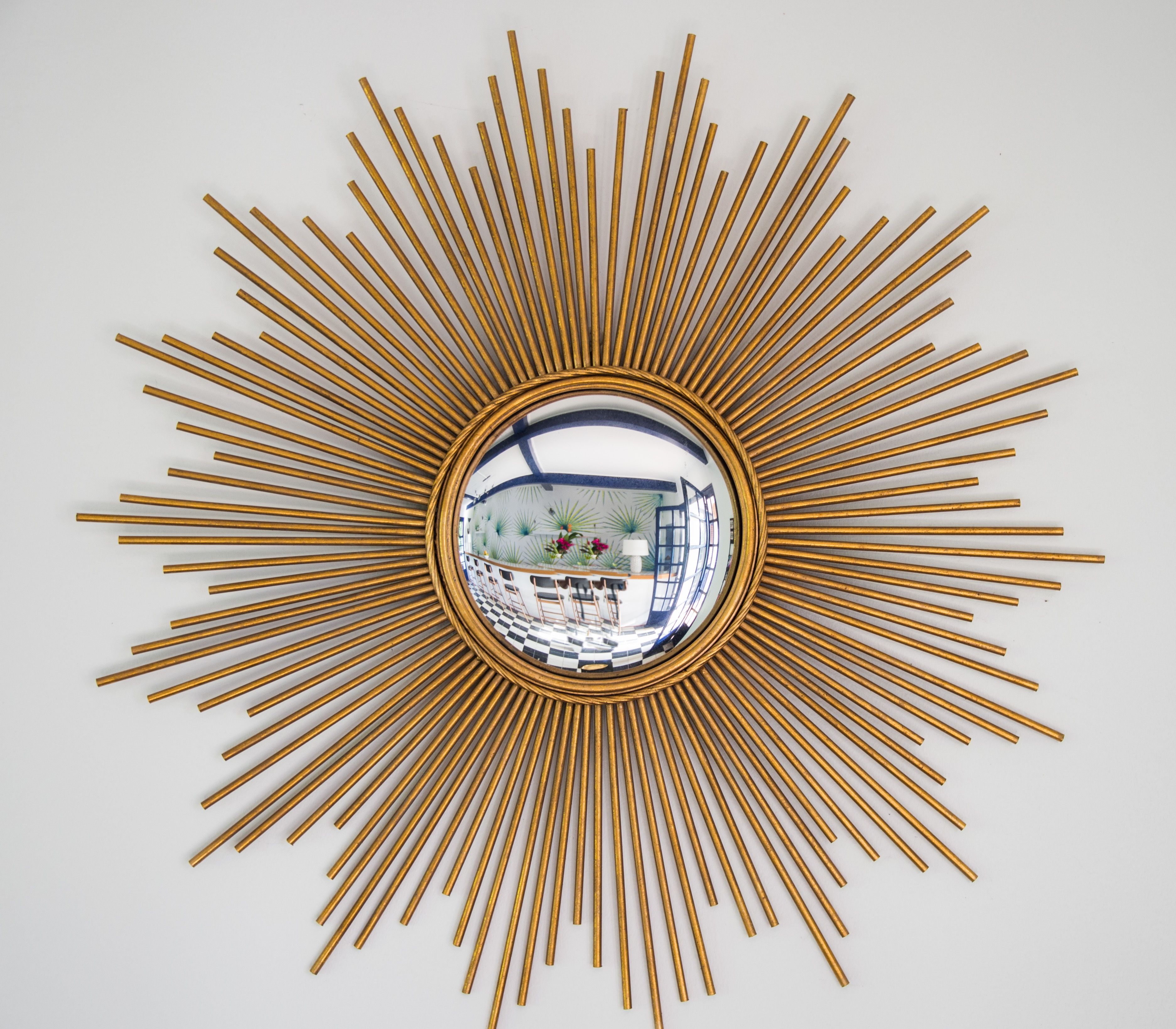 A sunburst mirror with a reflective center, surrounded by evenly spaced golden rods.