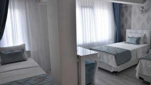 Habitación de hotel con dos camas, una mesita y un ventanal con cortinas traslúcidas.