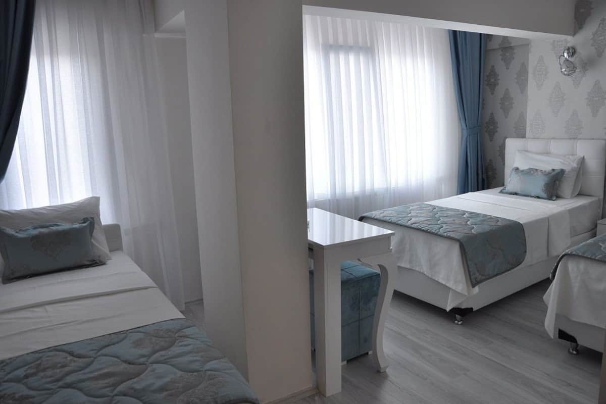 Habitación de hotel con dos camas, una mesita y un ventanal con cortinas traslúcidas.