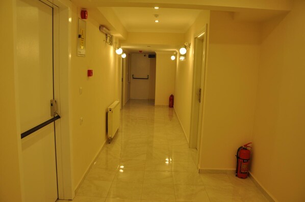 A narrow, well-lit hallway with a fire extinguisher on the right, a radiator on the left, and a door at the far end. - Hotel Iscen (Mustafakemalpasa)