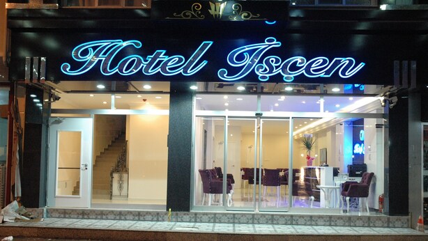 Entrada de un hotel con un letrero de neón, puertas de cristal y una escalera que da al interior.