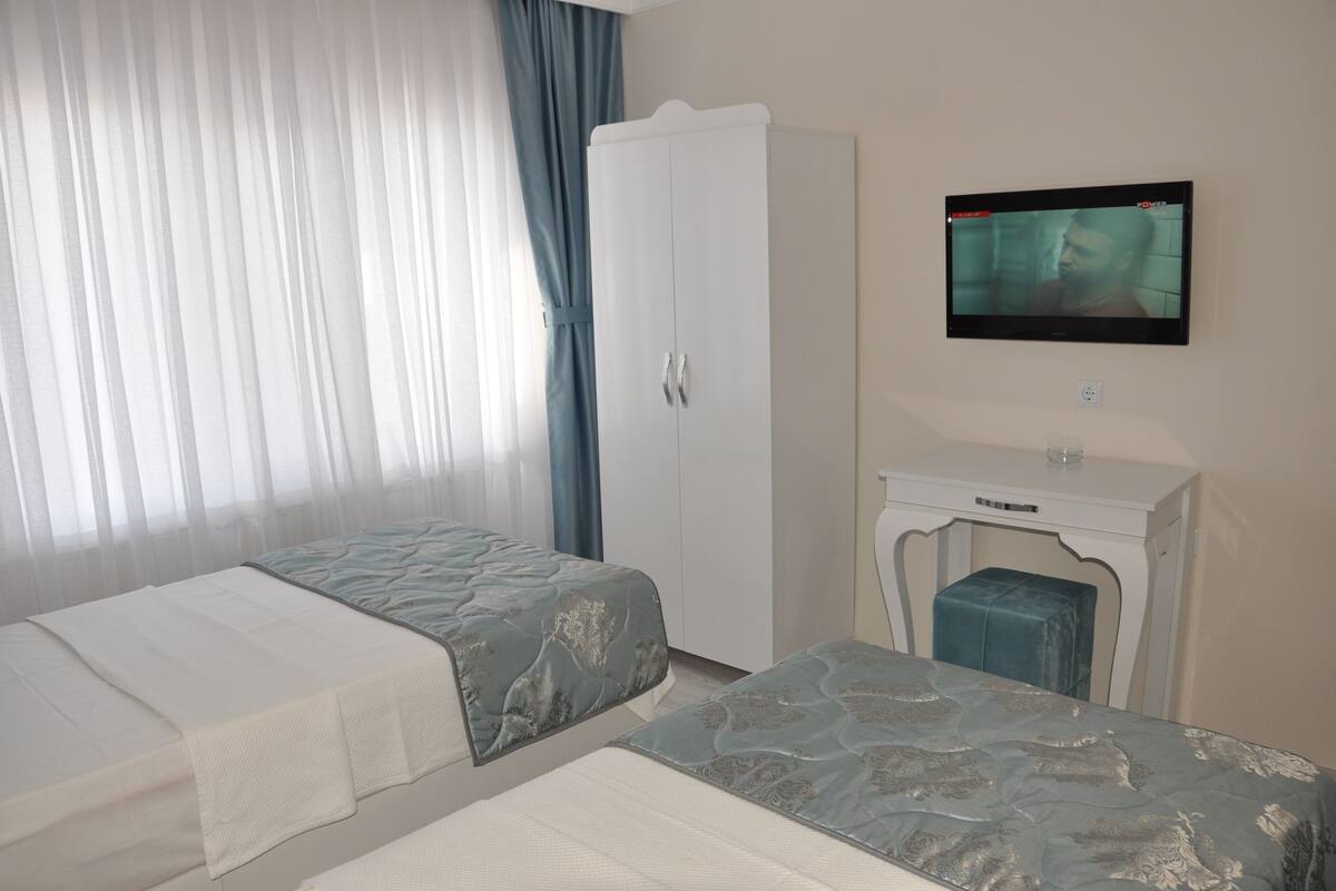 Una habitación de hotel con dos camas, un armario, un televisor y una mesita.