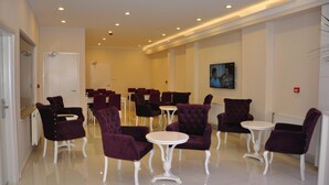 Un vestíbulo de hotel con filas de sillones morados y mesas blancas, un cuadro en la pared y una puerta al final de la habitación.