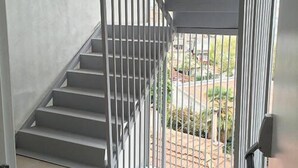 Una escalera con barandillas metálicas que lleva a un espacio al aire libre con vistas a un jardín y una calle.