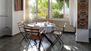 Uma sala de jantar com uma mesa redonda, seis cadeiras e vista para o verde lá fora.