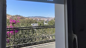 Placa com a inscrição 'Villa Tokur', mostrando uma vista de uma cidade no alto de uma colina e flores roxas.