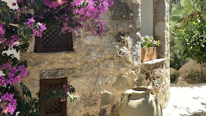 Um edifício de pedra com um grande vaso de barro, plantas em vasos e flores de bougainvillea roxas.