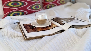 Uma cama com um livro, uma xícara de café e almofadas estampadas.