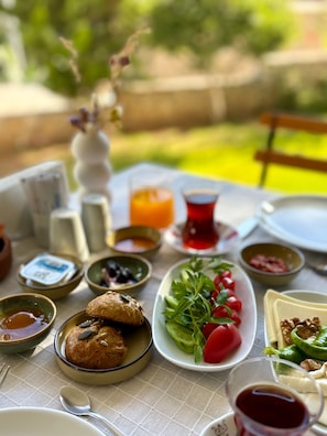 Taula ben posada amb diferents plats, com pa, verdures i condiments, a l'aire lliure amb un jardí desenfocat al fons.