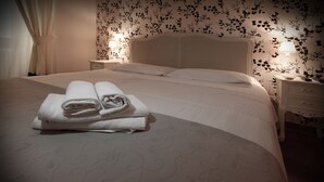 Cama bem arrumada com toalhas dobradas, cabeceira, abajures e um papel de parede estampado com motivos florais.