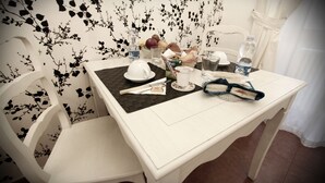 Uma mesa de jantar com toalha branca, apoio de mesa preto e diversos itens, incluindo um copo de água, uma garrafa de leite, um prato com uma xícara branca e uma cesta de pão.