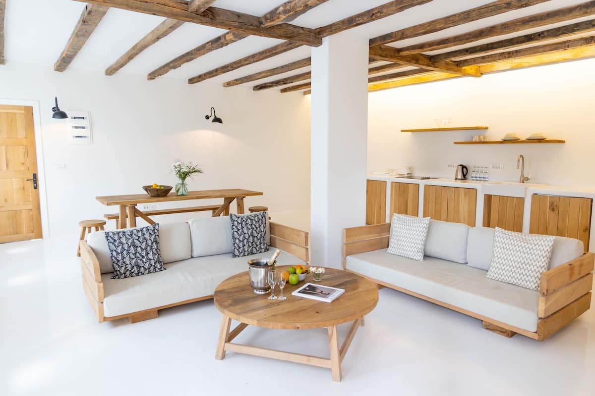 A modern living room with a wooden sofa, a round coffee table, and a kitchen area with wooden cabinets and a white countertop.