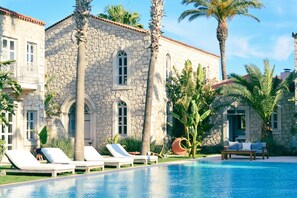 Un edificio de piedra con piscina, sillas de descanso y palmeras.