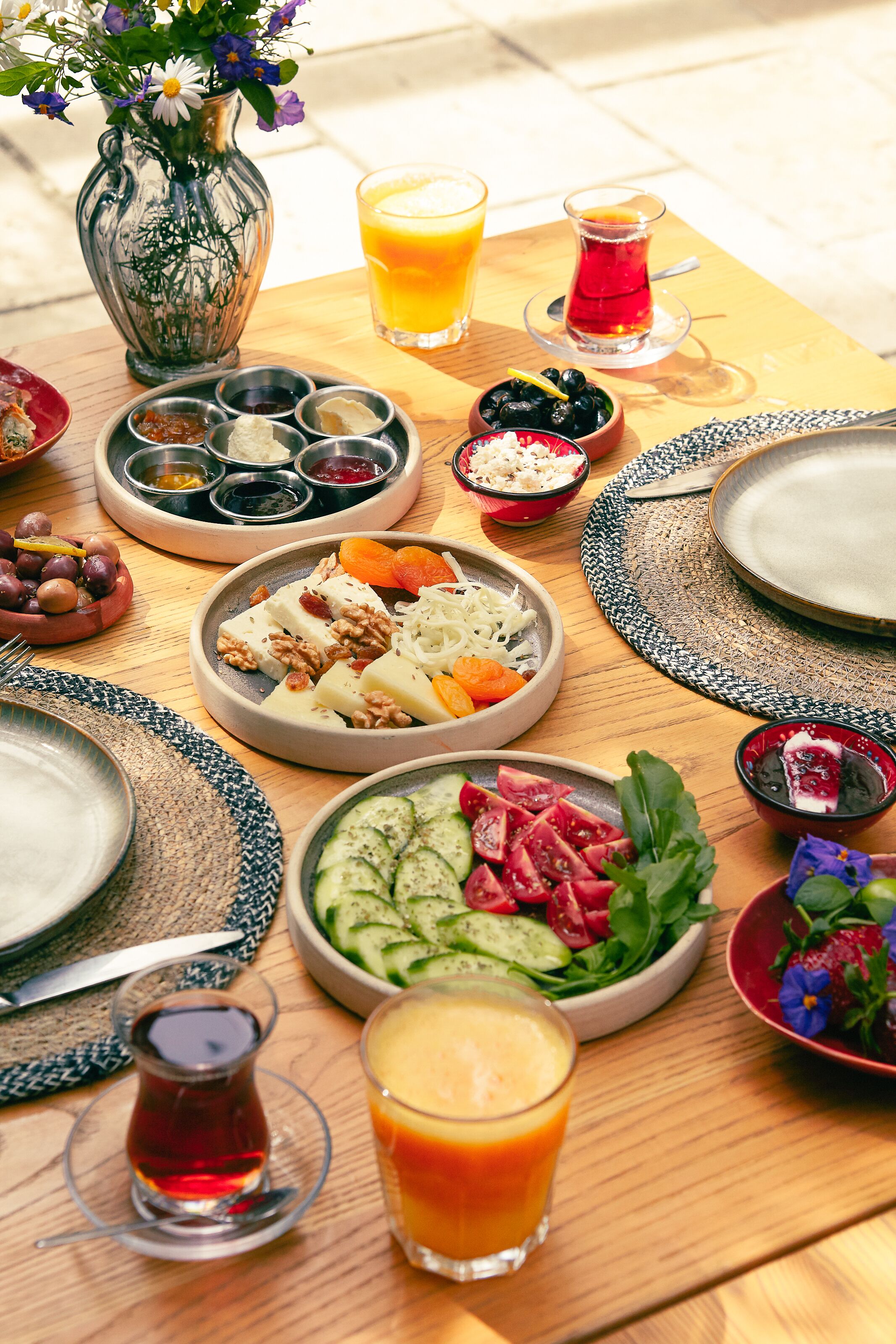 Una mesa de madera con diversos platos, entre ellos ensaladas, frutas y bebidas, dispuestas para una comida.