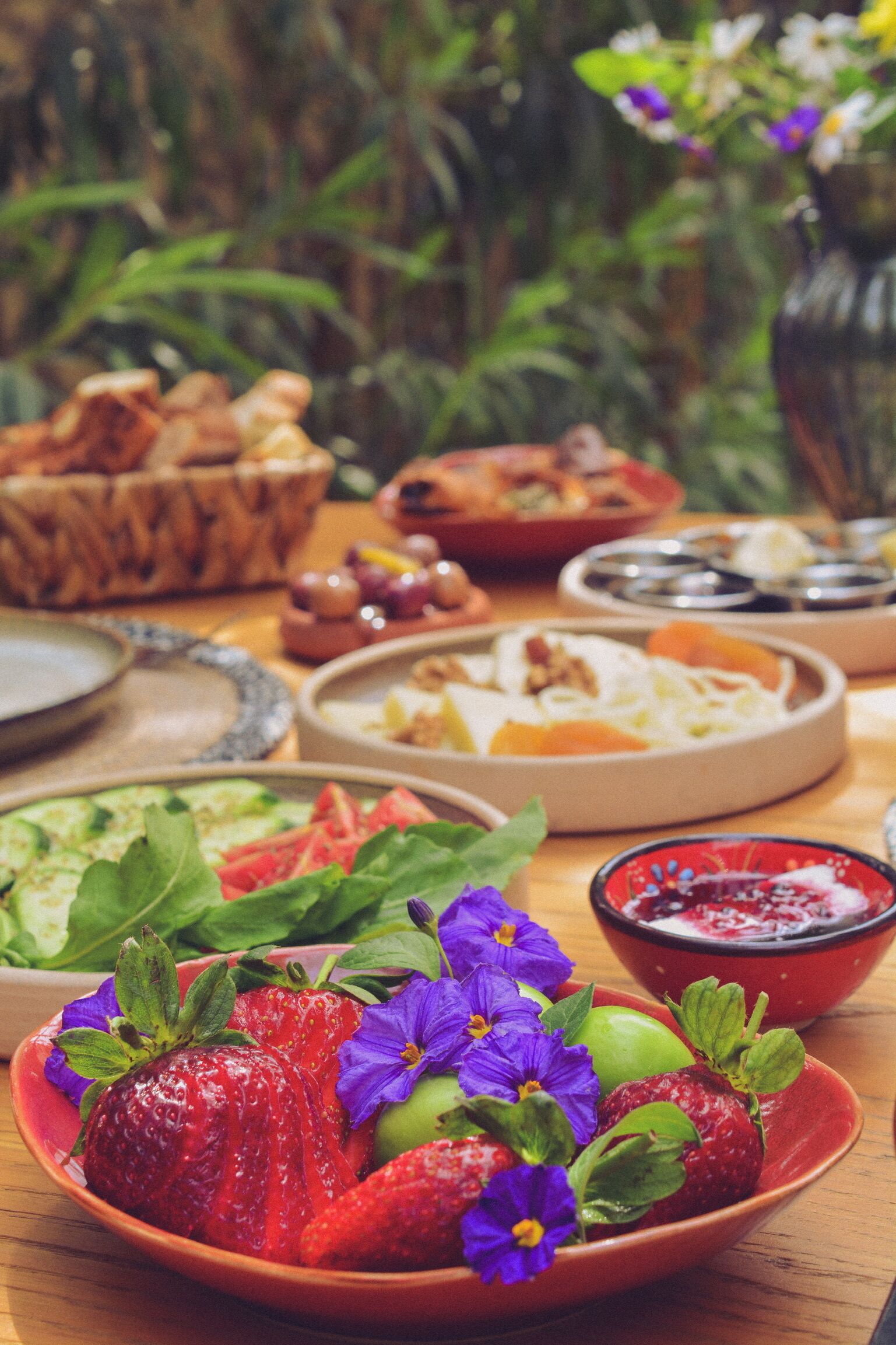 A table with various dishes, including a bowl of strawberries and flowers, and other food items.
