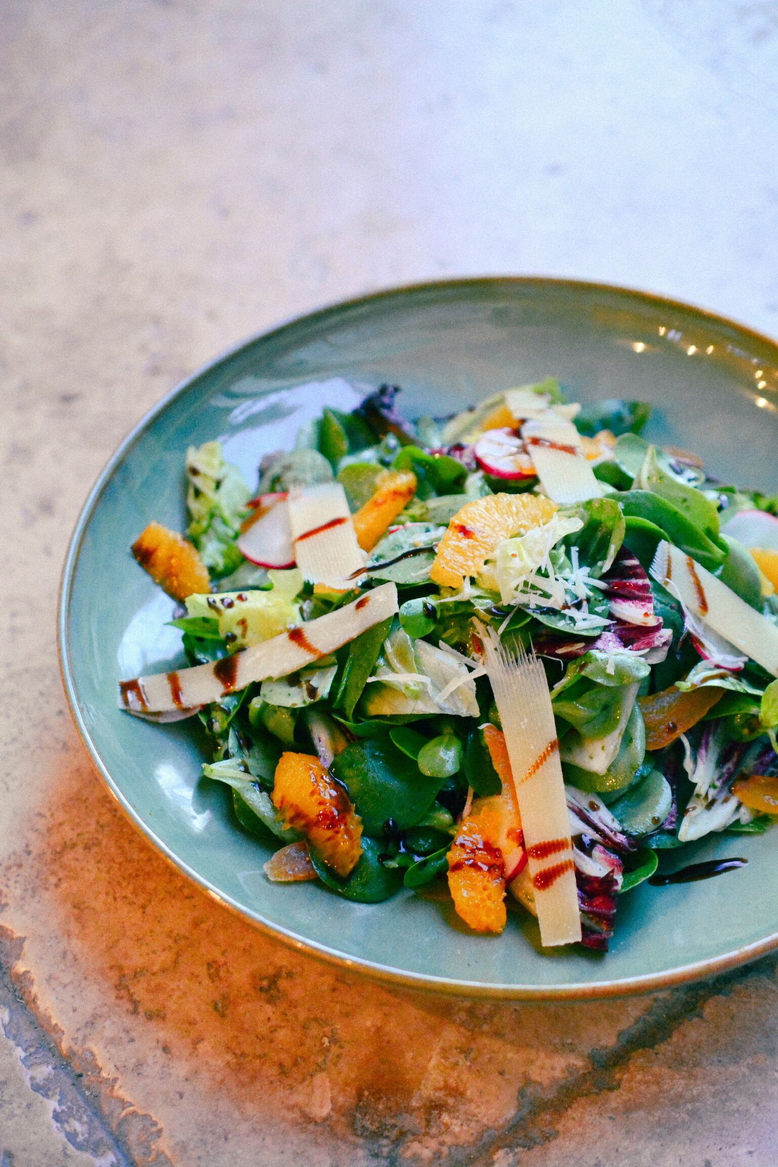 A plate of mixed greens salad with radishes, orange segments, and cheese.