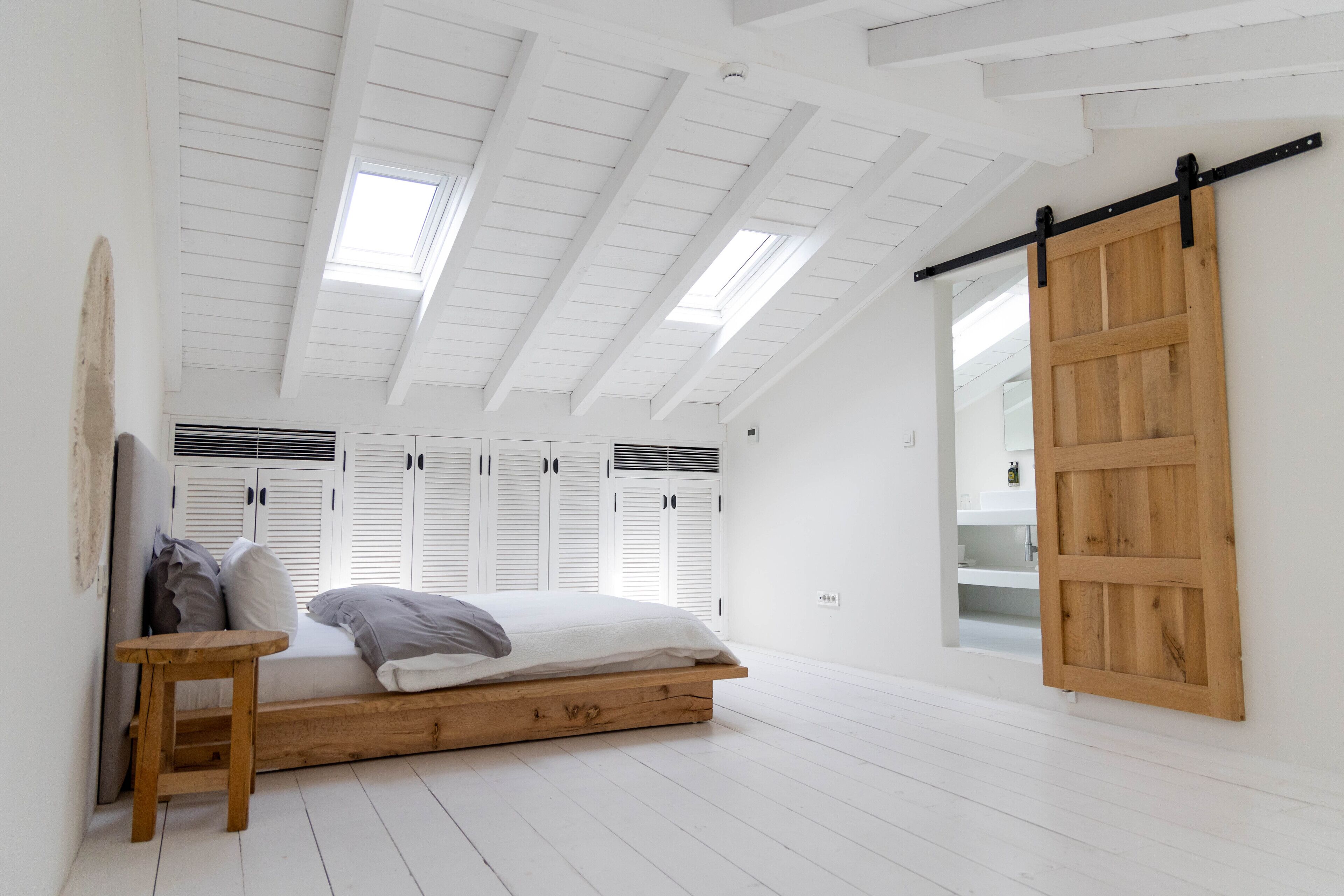 A bedroom with a loft bed, skylights, white walls, and a sliding barn door.