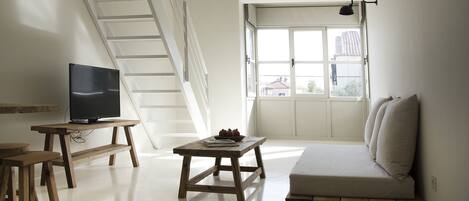 Una sala de estar moderna con un sofá, una mesa de centro de madera, un televisor sobre un mueble bajo y una escalera.