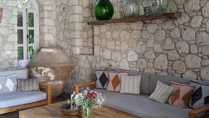 A stone-walled room with a wooden bench, a sofa, and a coffee table with a vase of flowers. - Manastir Alacati Hotel (Cesme)