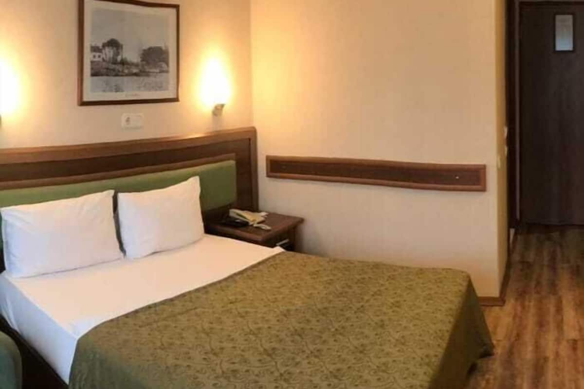A hotel room with a bed, a nightstand, a framed picture on the wall, and a door.