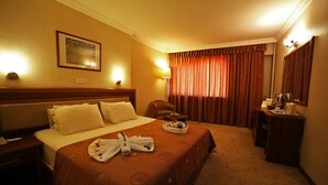 A hotel room with a large bed, a desk with a chair, a lamp, and a painting on the wall. - Hotel Villa Marina (Bandirma)