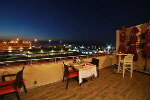 Un área de comedor en la azotea con una mesa dispuesta para dos, con vistas a un paisaje urbano nocturno.