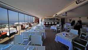 A restaurant with tables set for dining, a bar area, and a view of the sea. - Hotel Villa Marina (Bandirma)