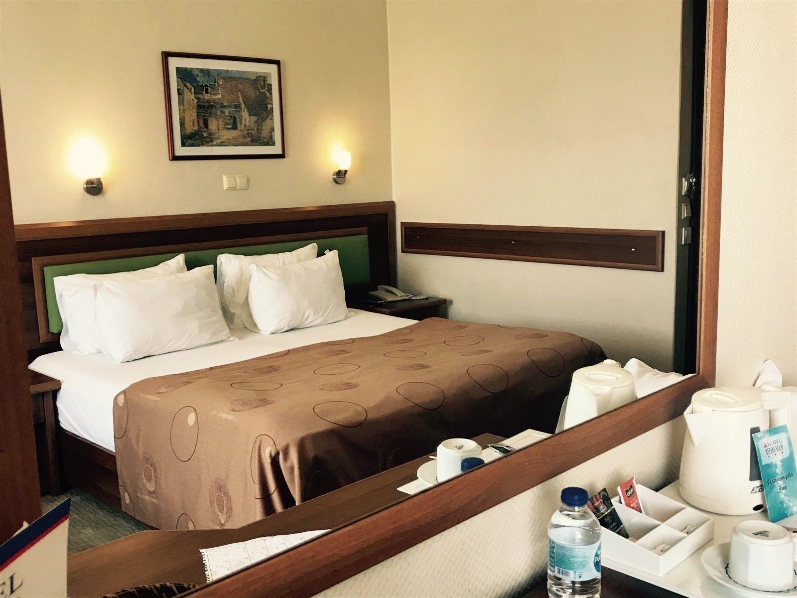 Una habitación de hotel con una cama, una mesita de noche, una lámpara y un cuadro en la pared, además de una ventana con cortinas.