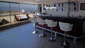 A modern bar area with a view of the sea and mountains, featuring bar stools, a wine and liquor display, and a large window. - Hotel Villa Marina (Bandirma)