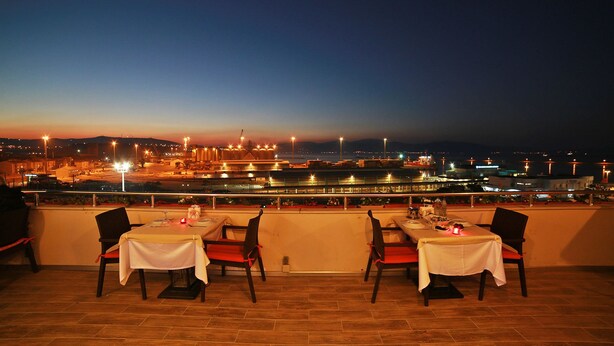 A rooftop dining area with tables set for two, overlooking a cityscape at dusk. - Hotel Villa Marina (Bandirma)