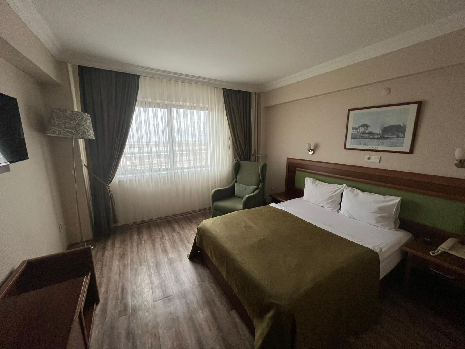 A hotel room with a bed, a chair, a desk, a lamp, and a window with curtains.