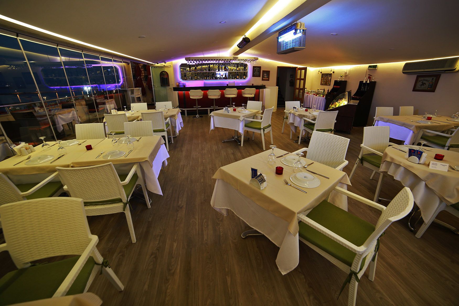 A restaurant with multiple tables and chairs, a bar area, and a view of the cityscape through large windows.