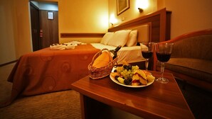 A hotel room with a bed, a bedside table with a basket, a plate of fruit, and two glasses of red wine. - Hotel Villa Marina (Bandirma)