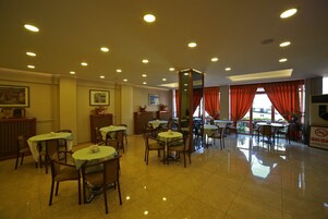 Um restaurante com várias mesas e cadeiras, piso ladrilhado e teto com iluminação embutida.