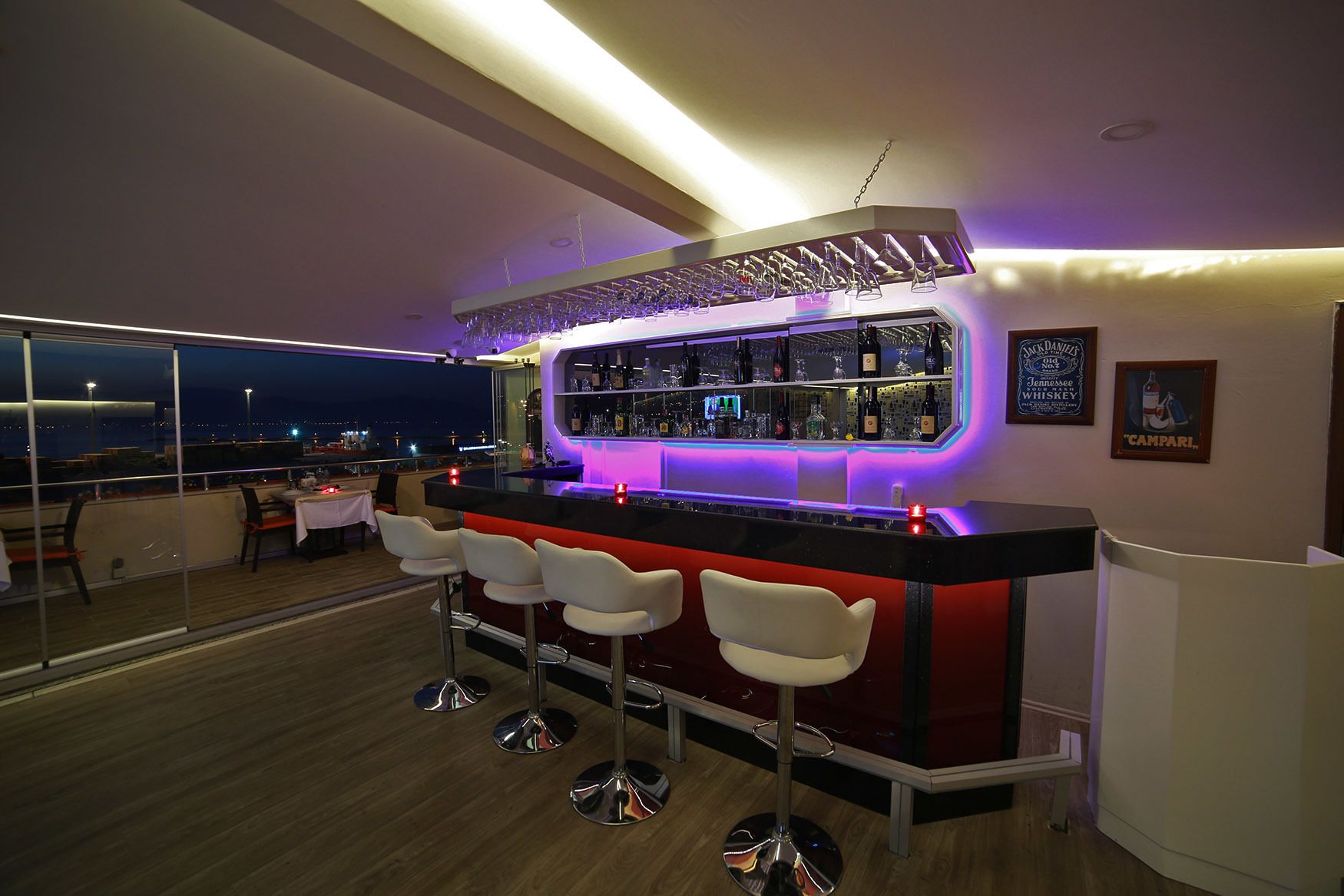 Eine moderne Bar mit einer roten Theke, Barhocker und Blick auf die beleuchtete Stadt bei Nacht.