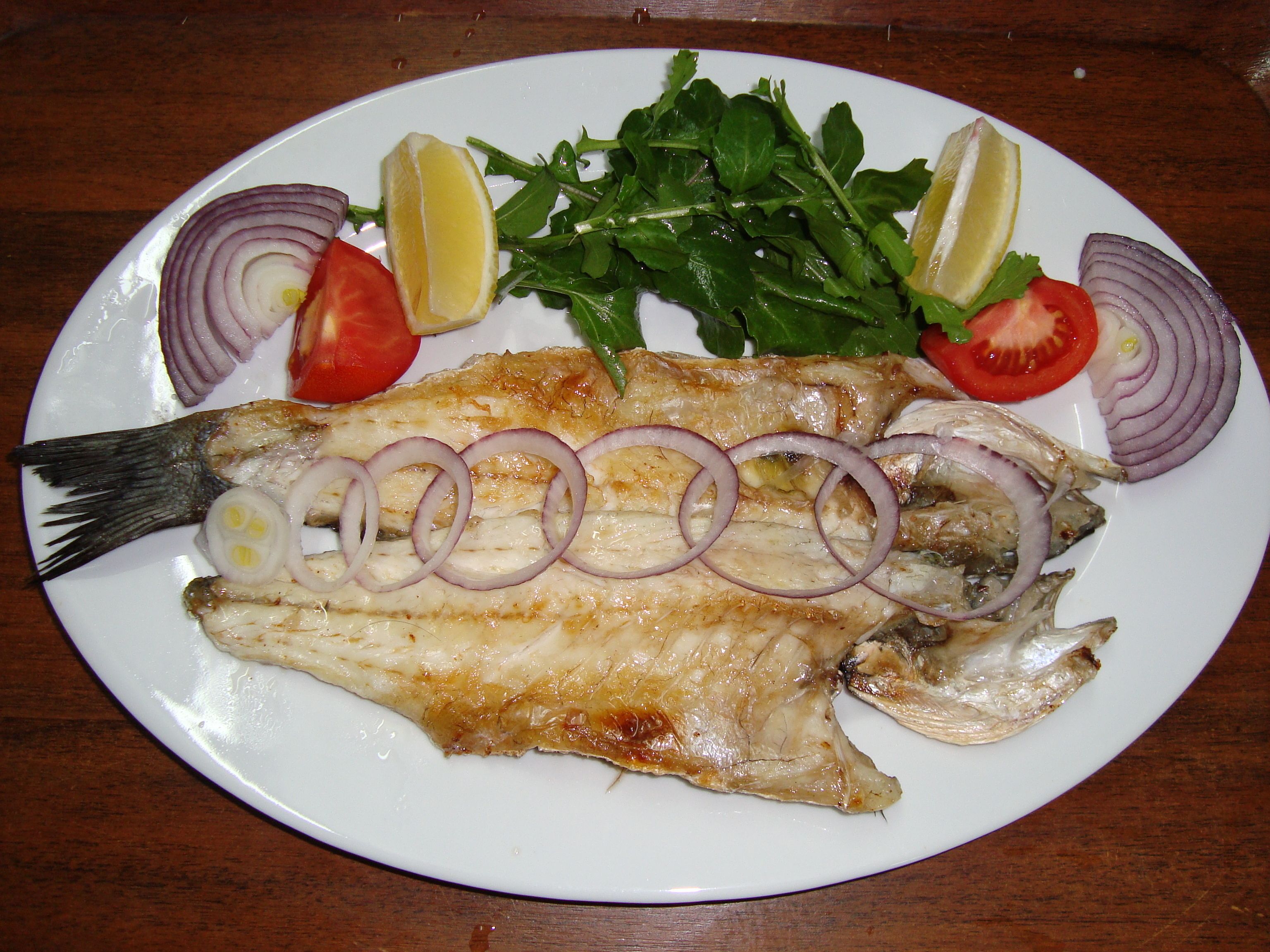 A plate with grilled fish, lemon slices, tomato, and onion rings.