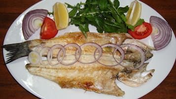A plate with grilled fish, lemon slices, tomato, and onion rings.