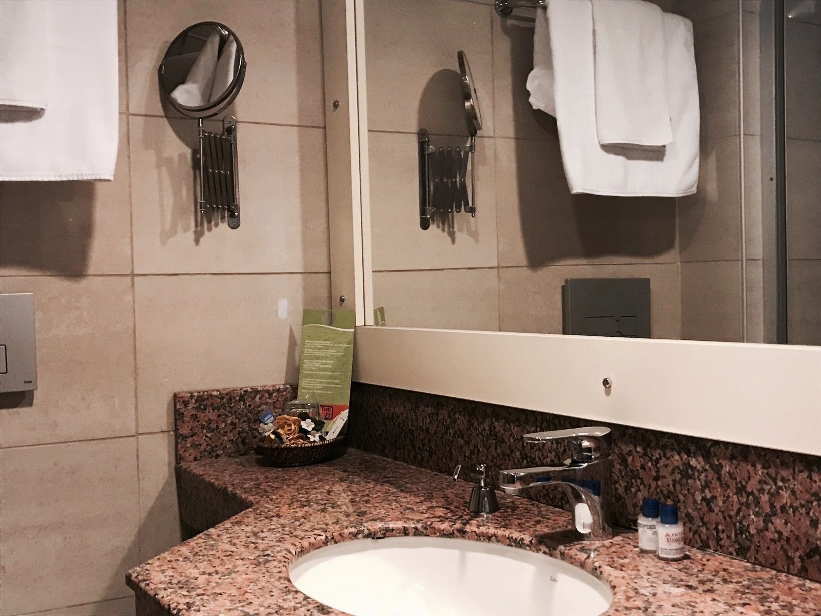 Un baño con encimera de granito, un lavamanos, un espejo y un perchero para toallas.