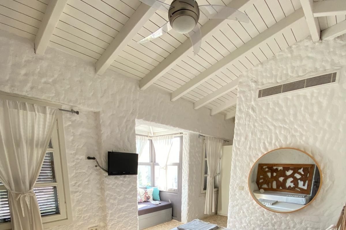 A bedroom with a bed, a ceiling fan, a TV, and a window with curtains.
