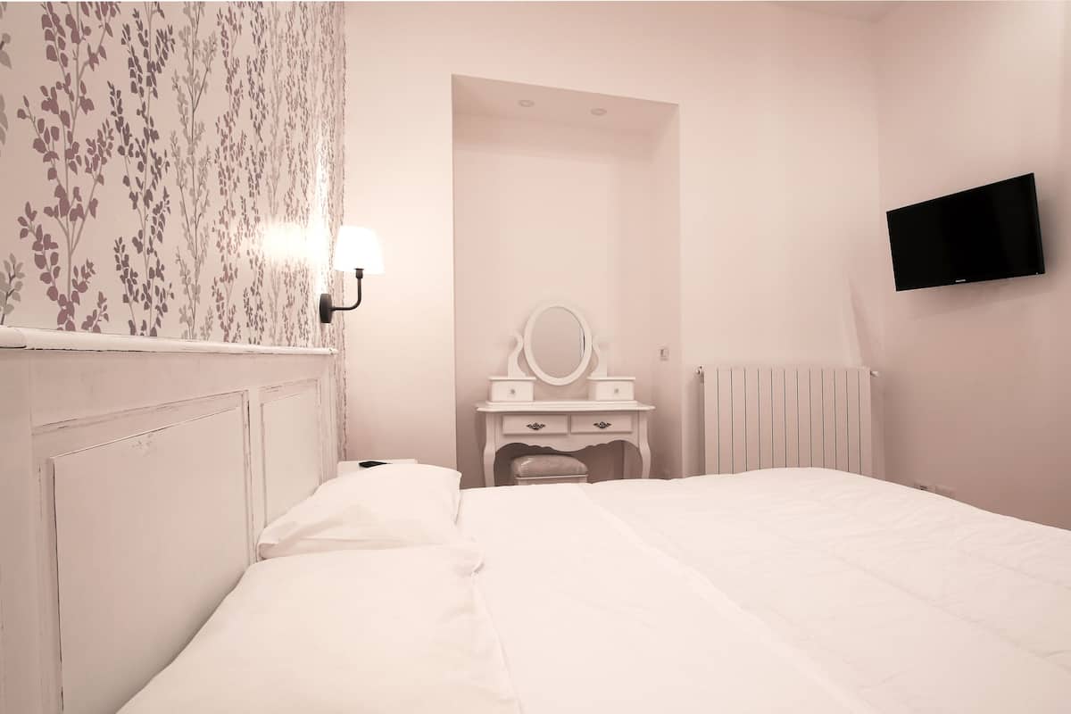 A bedroom with a bed, a vanity with a mirror, a television on the wall, and a radiator.