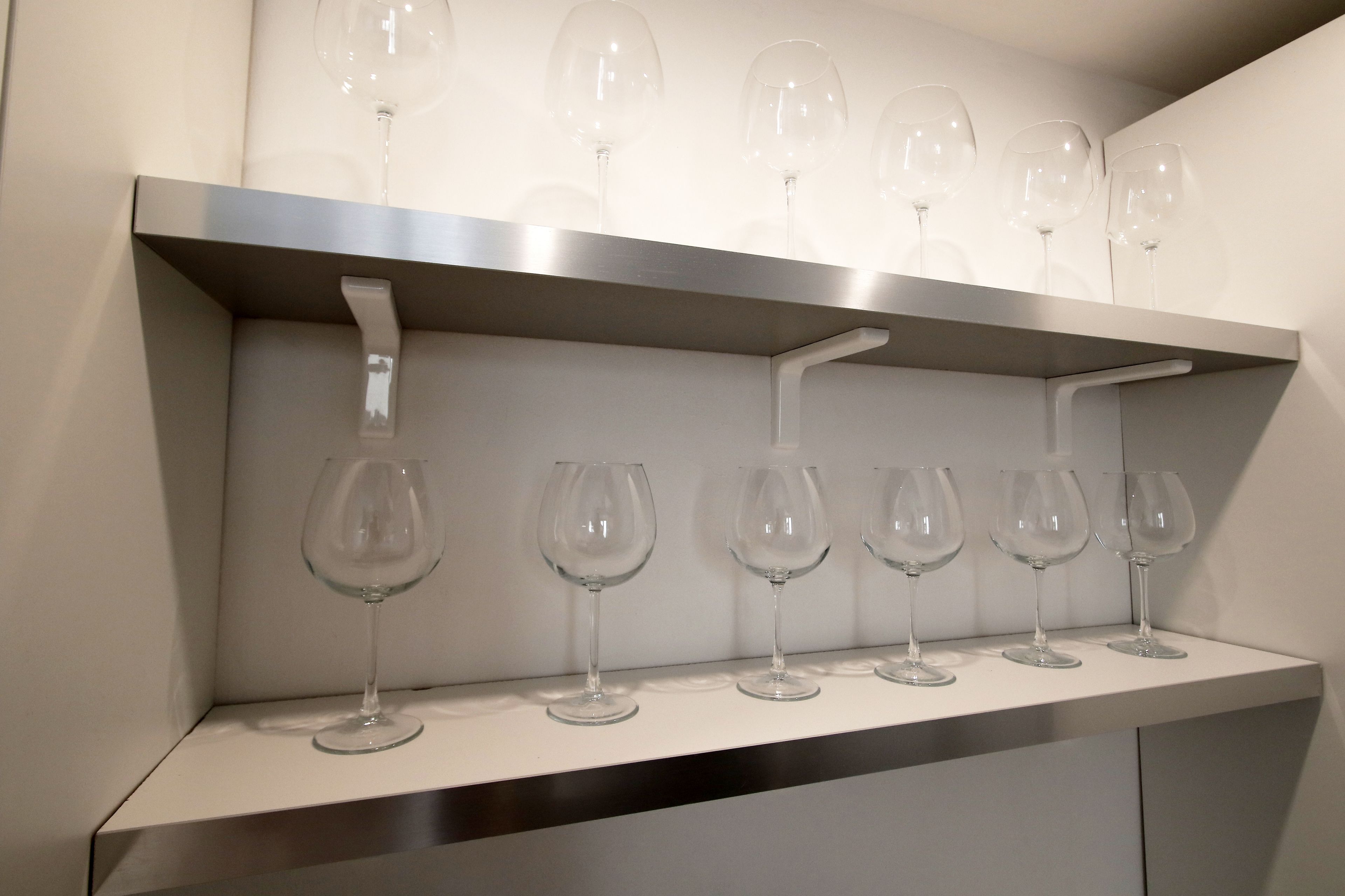 Une étagère blanche sur laquelle sont disposés six verres à vin, alignés en deux rangées.