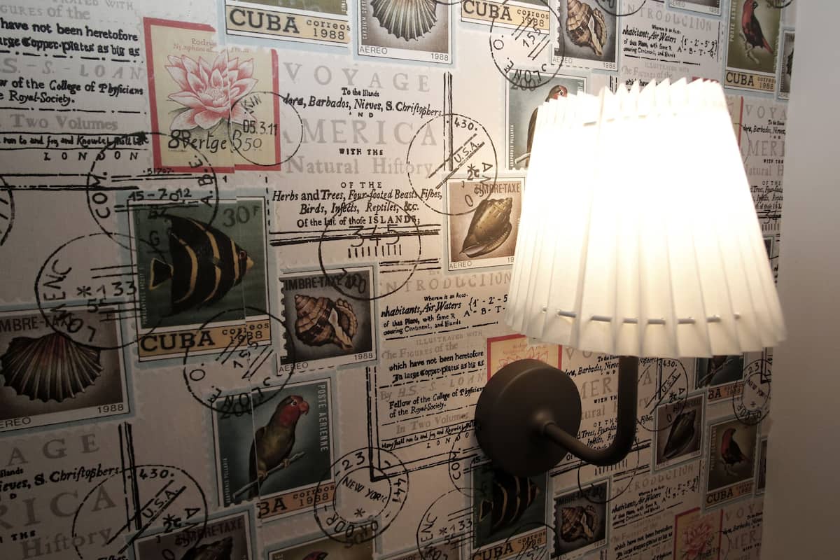 A wall with vintage stamps and postcards, a lamp, and a bird figurine.