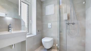 A modern bathroom with a glass shower enclosure, a white toilet, and a sink with a window above.