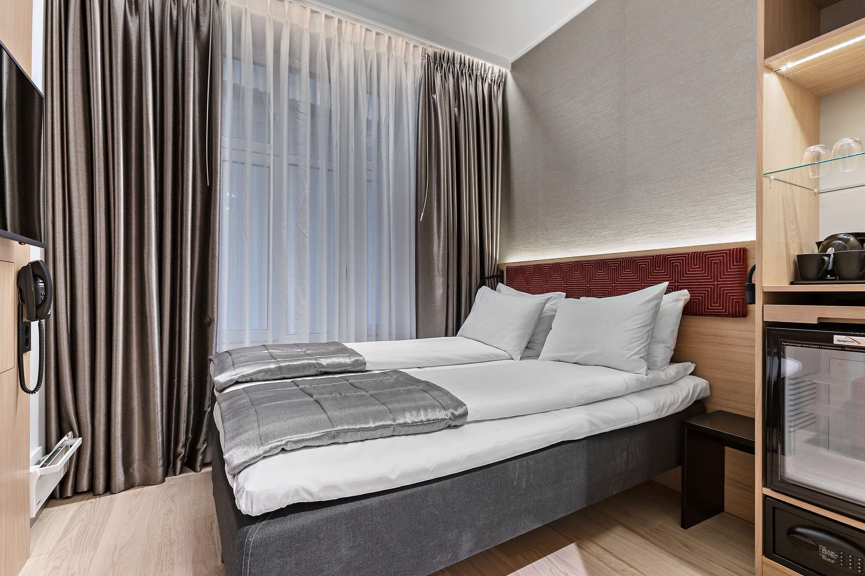 A hotel room with a bed, curtains, a TV, a small table, and a microwave.