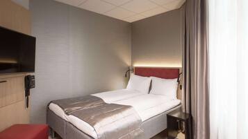 A hotel room with a bed, a bedside table, a TV, a phone, and a red bench.