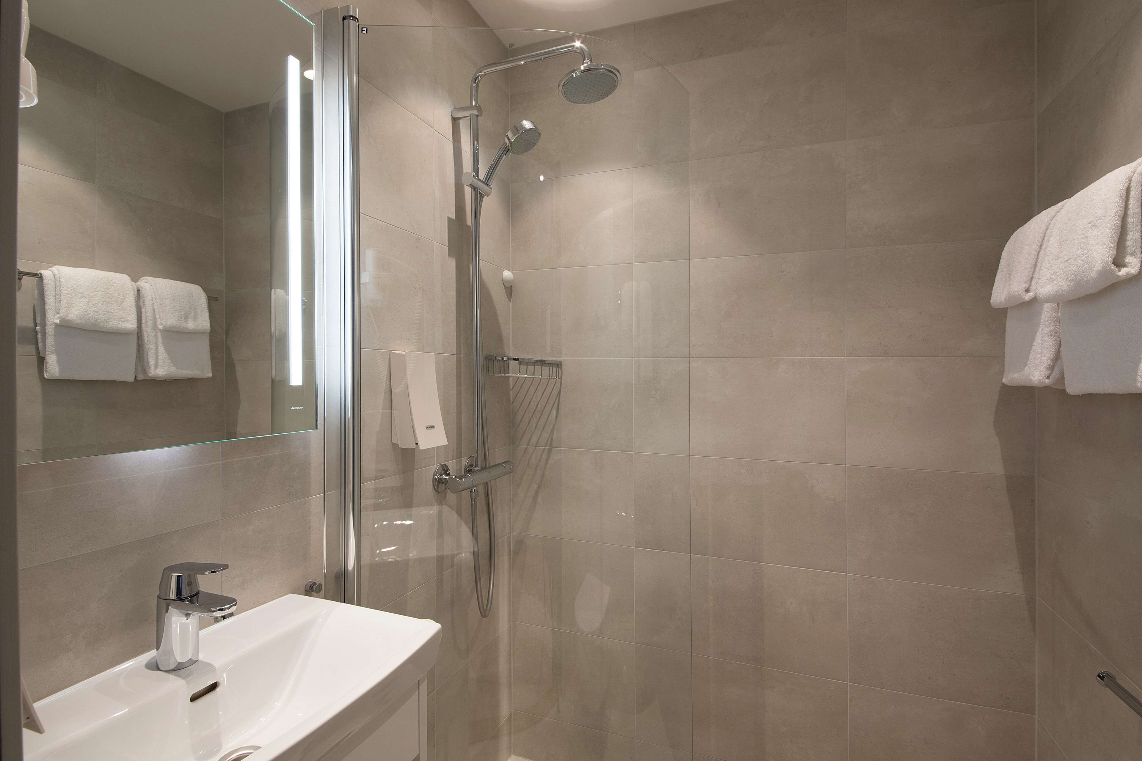 A modern bathroom with a glass-enclosed shower, a white sink, and a large mirror.