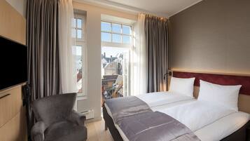 Ein Hotelzimmer mit Bett, Sessel, Fernseher und einem fenster mit Vorhängen.