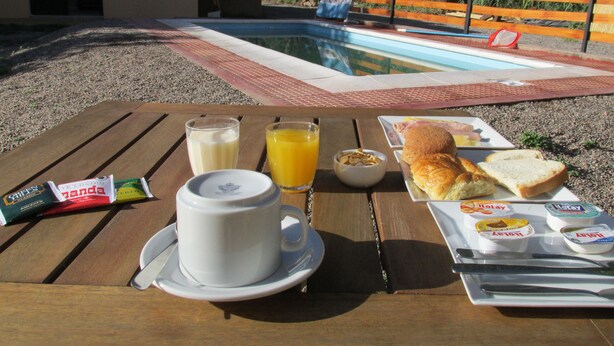 Une table en bois dressée pour le petit-déjeuner, avec une tasse, du jus, du pain et une assiette contenant des œufs et du jambon.