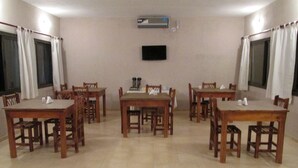 Un coin repas avec des tables et des chaises en bois, un téléviseur à écran plat fixé au mur et un appareil de climatisation placé au-dessus du téléviseur.
