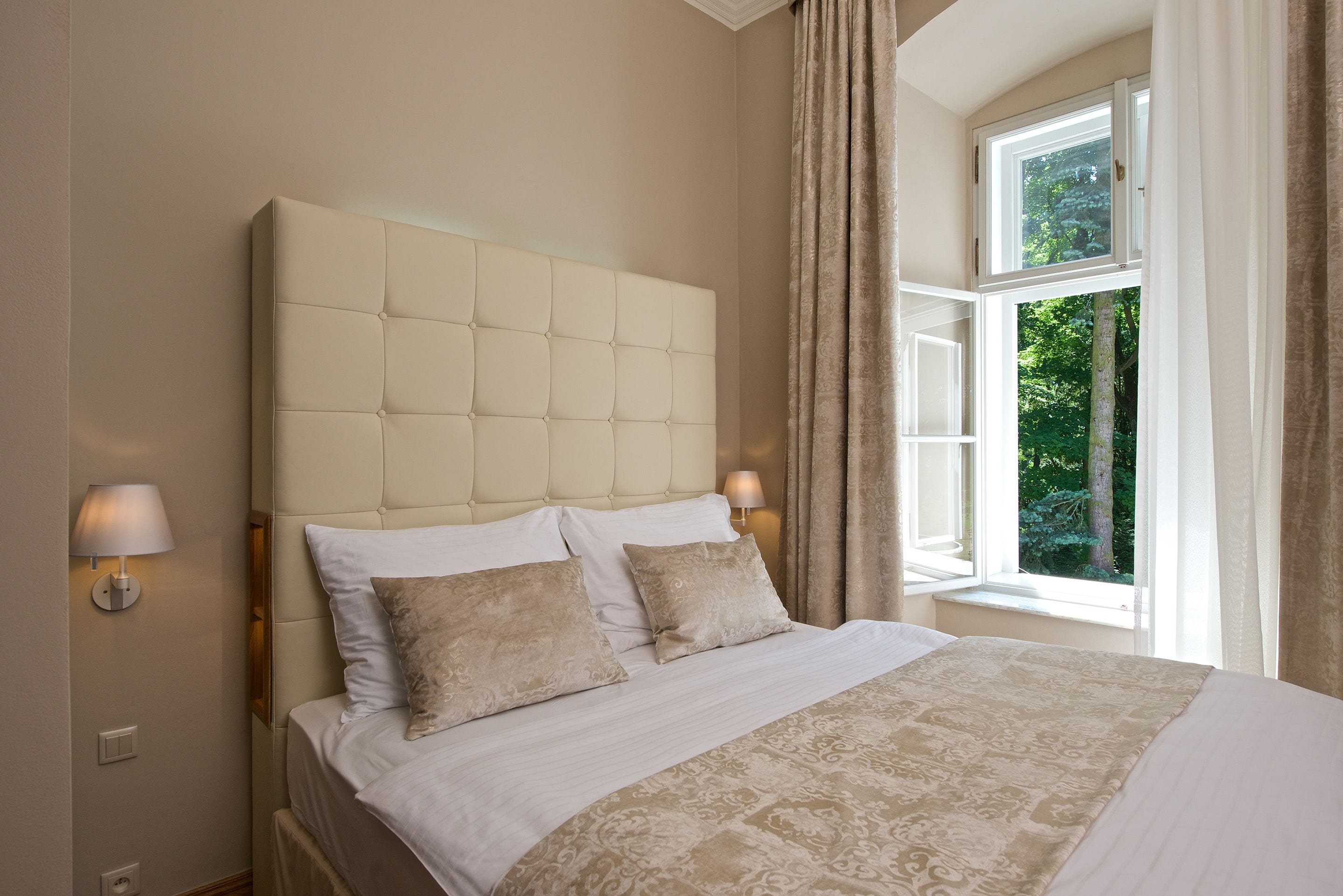 Quarto com uma cama grande, duas luminárias de cabeceira e uma janela com cortinas.